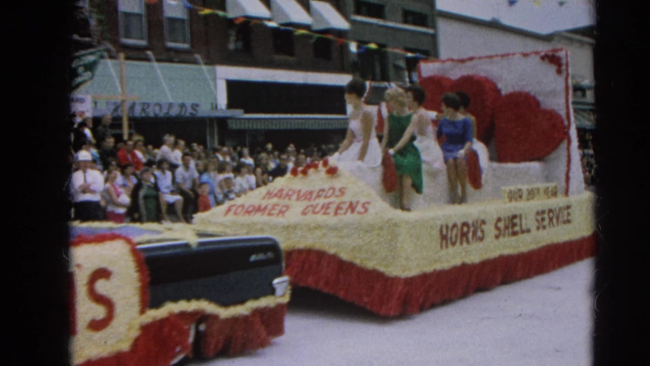 1964 Harvard, Illinois parade float labeled Harvard's Former Queens and Horn's Shell Service passes a crowded downtown street.