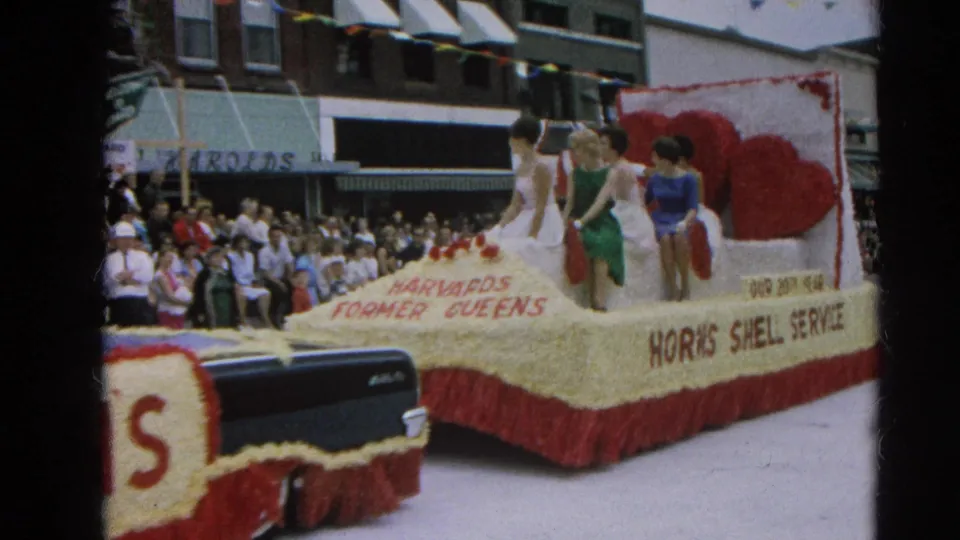 1964 Harvard, Illinois parade float labeled Harvard's Former Queens and Horn's Shell Service passes a crowded downtown street.