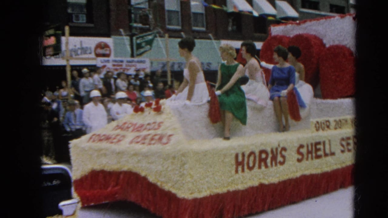 Decorated float with red hearts and women in dresses moves past the crowd.