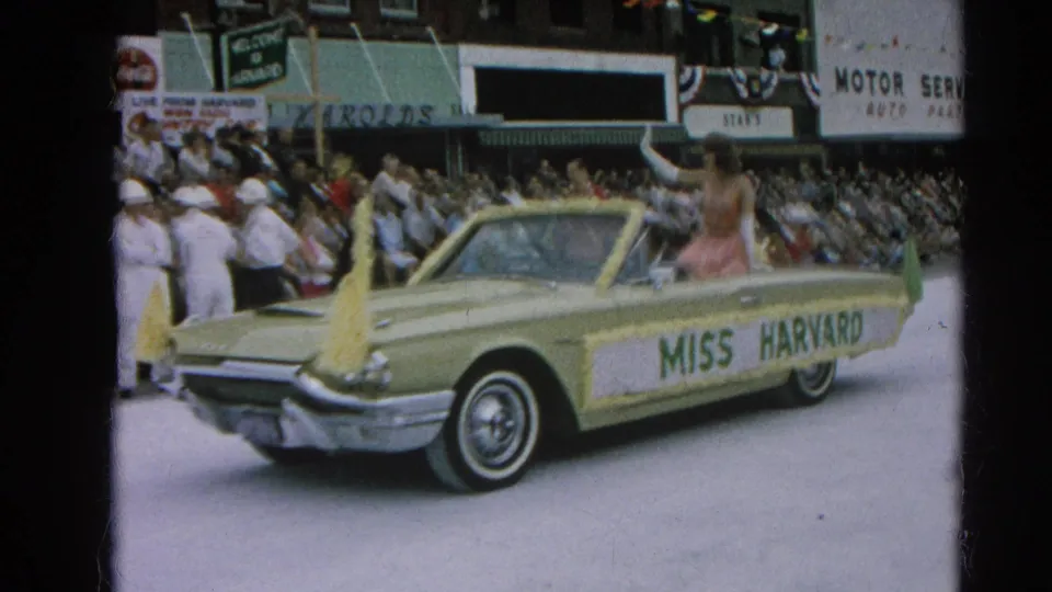 A classic convertible with Miss Harvard lettering carries a waving participant past downtown spectators in the 1964 Harvard, Illinois parade.