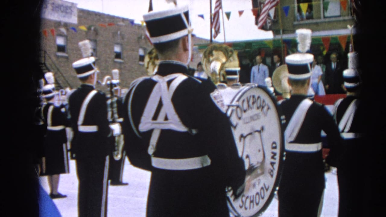 Marching band members in black and white uniforms stand near a large bass drum.
