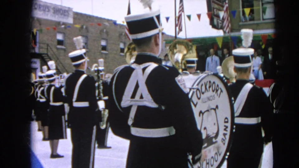 Lockport High School Band members proceed through a Harvard, Illinois parade in 1964, filmed from behind on 8mm.
