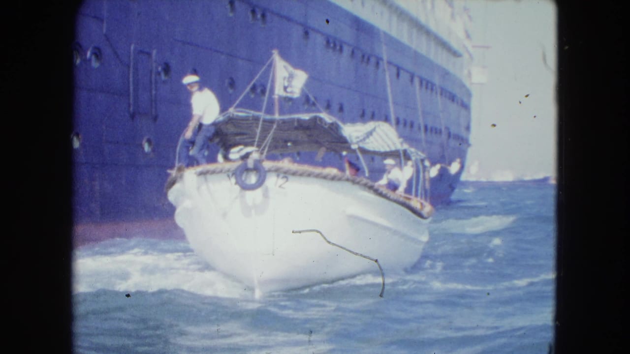 1964 Kingston, Jamaica footage shows a small white launch rocking beside a dark ocean liner hull with a sailor at the bow.