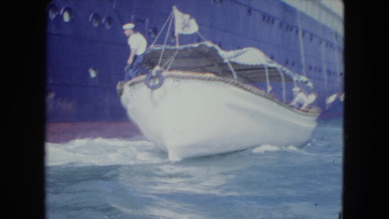 Bow of a white launch rises through waves next to the dark side of a larger vessel.
