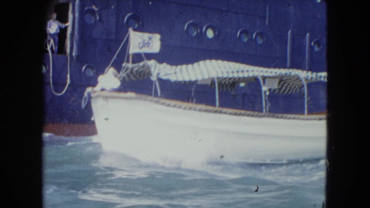 White harbor boat beside a large ocean liner in Kingston, Jamaica, with portholes, doorway observer, and choppy blue water visible.