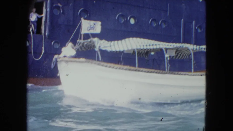 White harbor boat beside a large ocean liner in Kingston, Jamaica, with portholes, doorway observer, and choppy blue water visible.