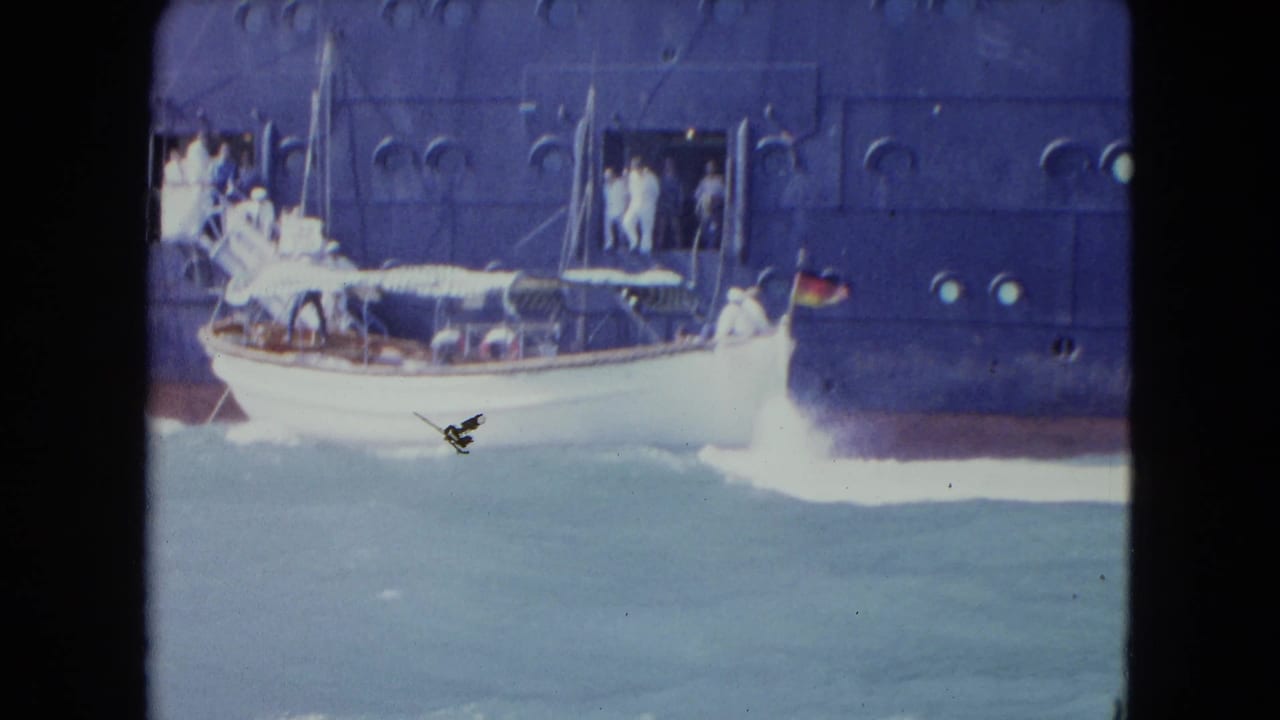 In 1964 Kingston, Jamaica, a small white motorboat passes alongside a dark blue ocean liner as people stand near an open side doorway.