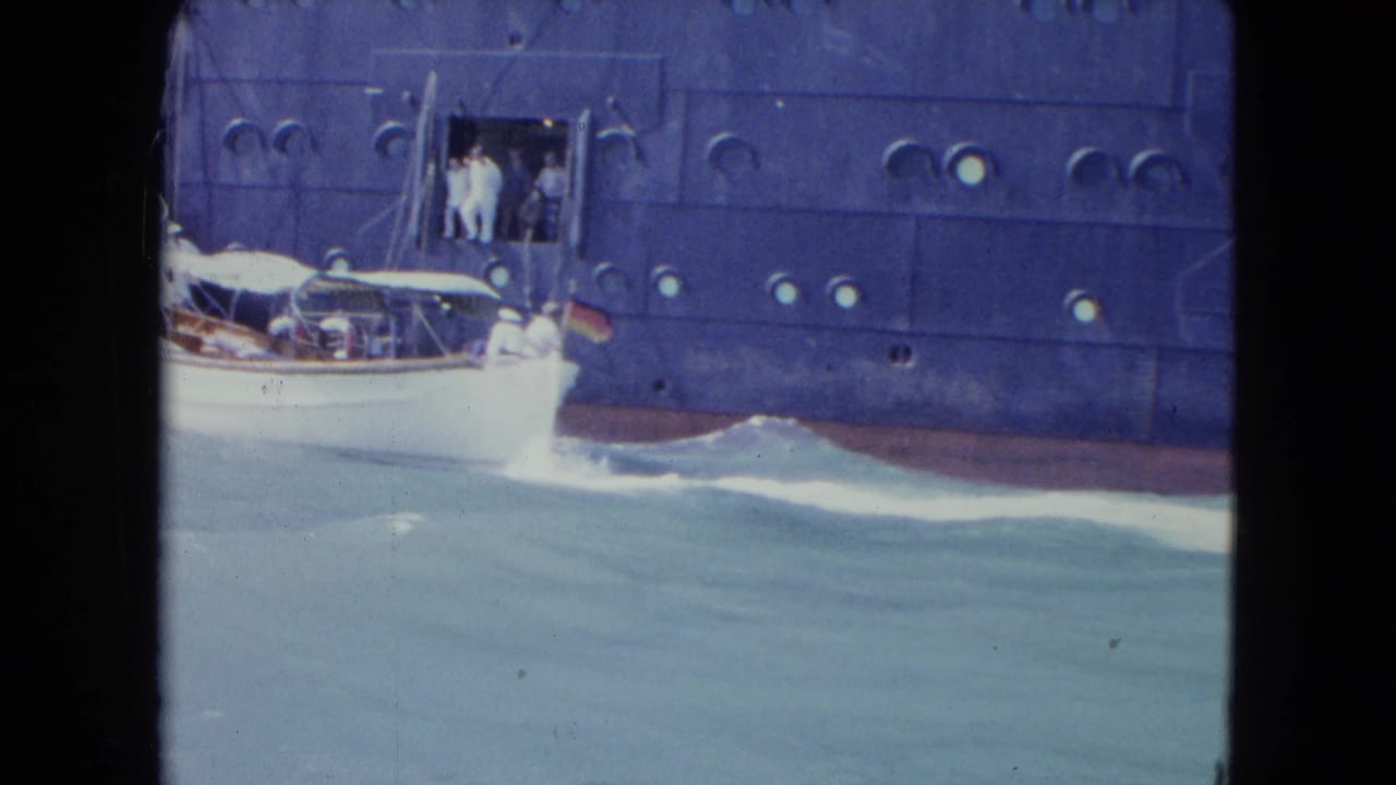 The white motorboat draws level with the ocean liner in Kingston, Jamaica, with people visible at the side opening and wake along the hull.