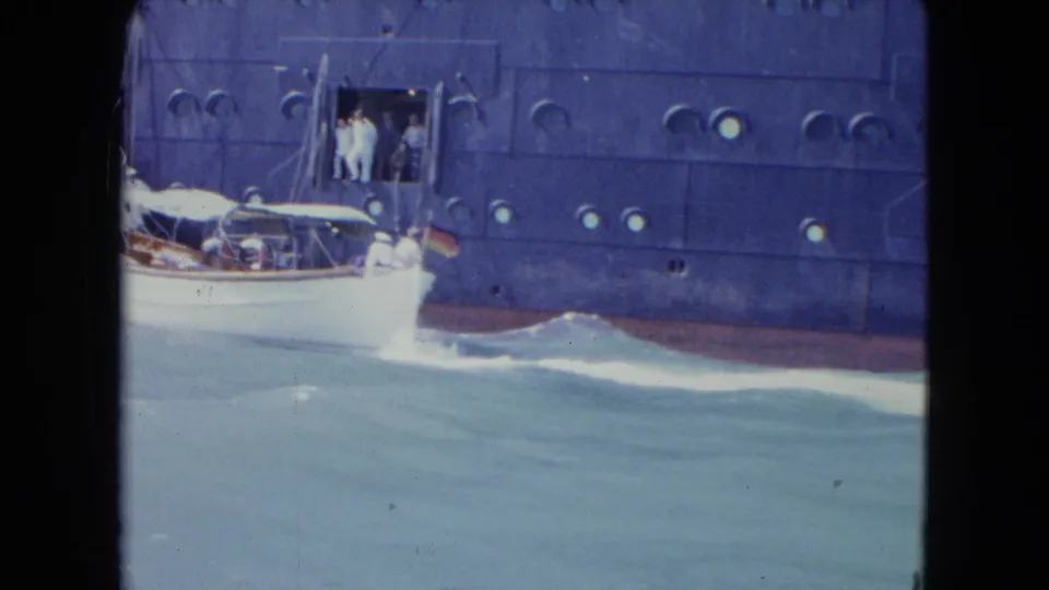 The white motorboat draws level with the ocean liner in Kingston, Jamaica, with people visible at the side opening and wake along the hull.