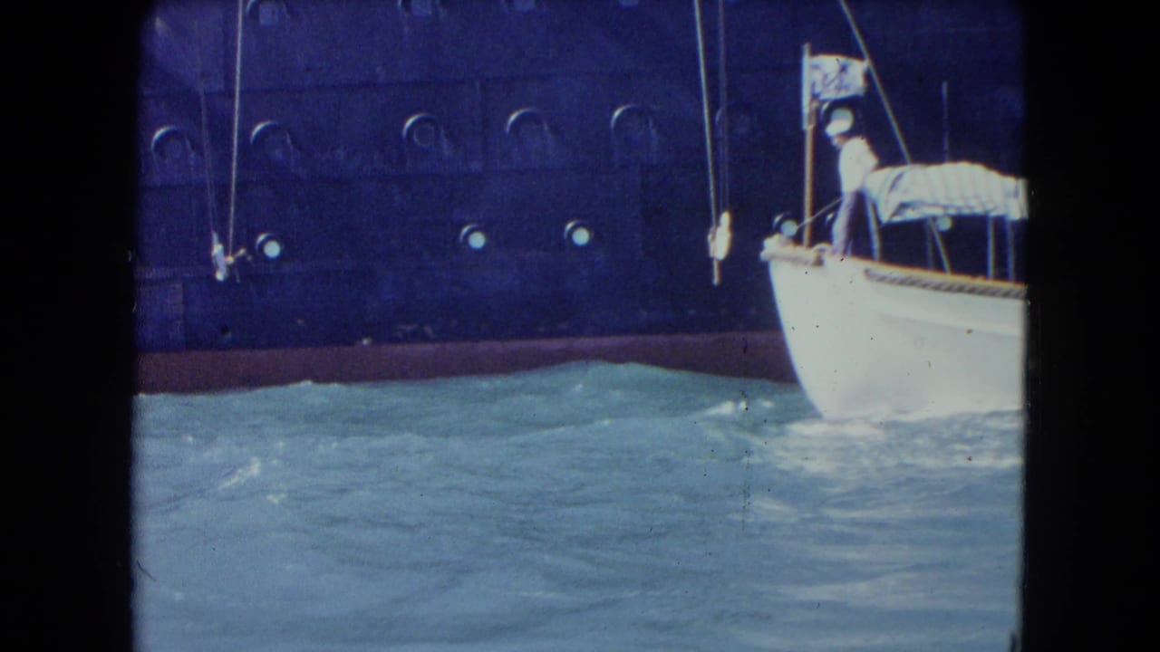 Small white boat entering frame beside a dark ship hull in choppy water.
