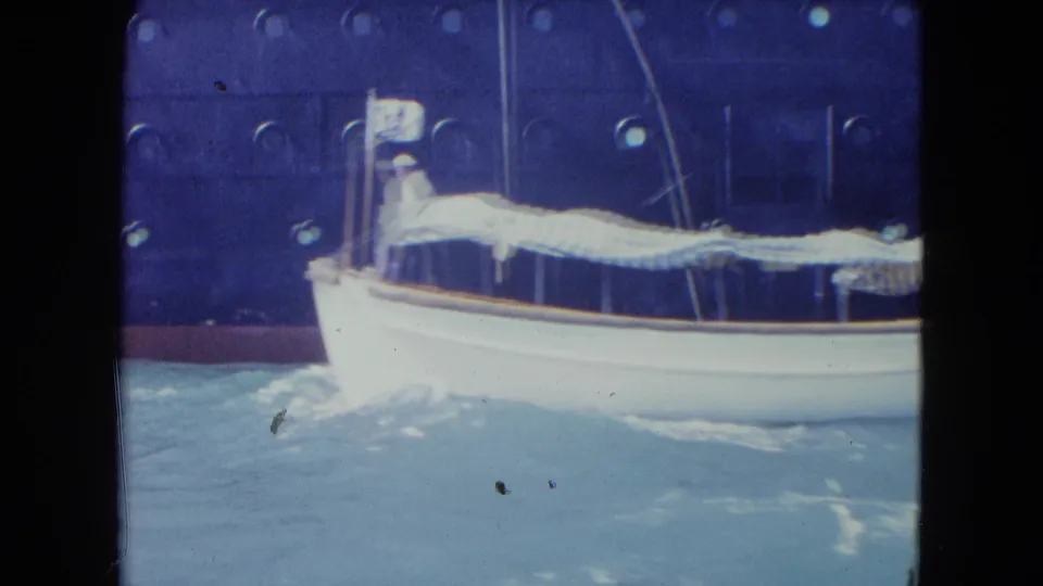 A white launch with a striped canopy rolls in Kingston harbor water, with a dark porthole-lined ship hull behind it.