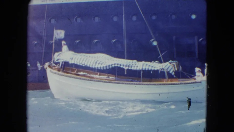 Broadside 8mm view of the small Kingston boat under a striped awning as crew figures remain visible in rough harbor water.