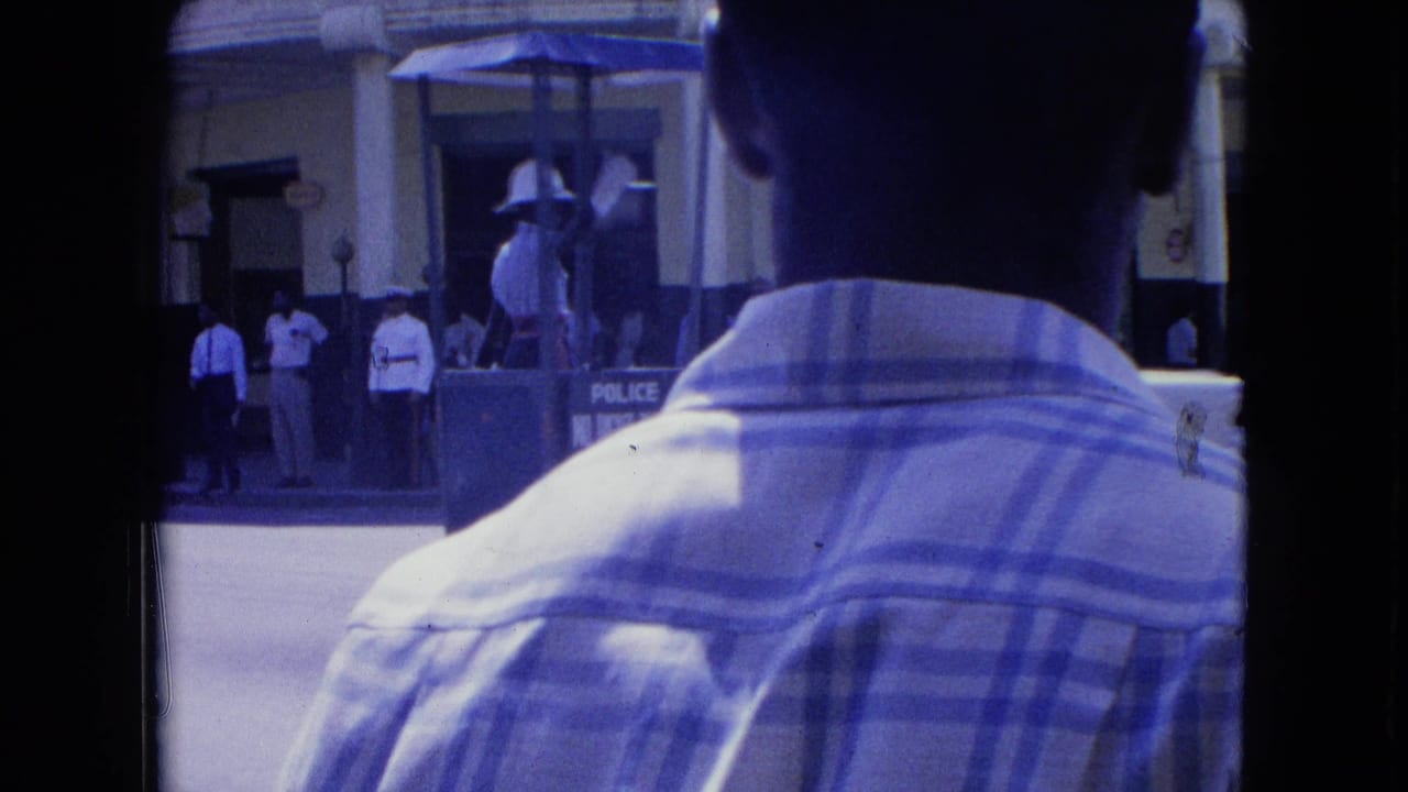 1964 Kingston street view from behind a plaid-shirted man, with a white-uniformed police officer in a raised traffic booth near Yellow House.