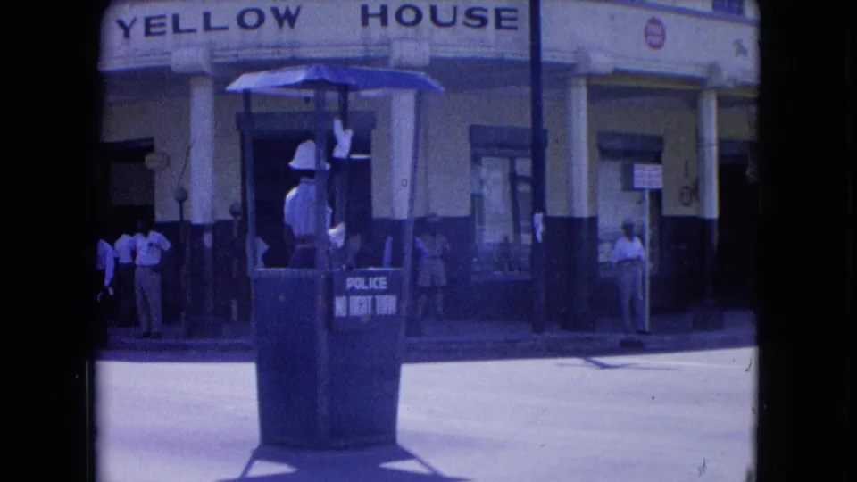 The Yellow House frontage is clearer as a white-uniformed Kingston traffic officer stands in a raised police booth with pedestrians nearby.