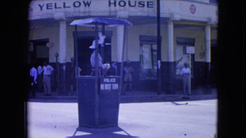 A Kingston traffic officer appears to gesture from a raised police booth outside Yellow House, with pedestrians along the sidewalk.