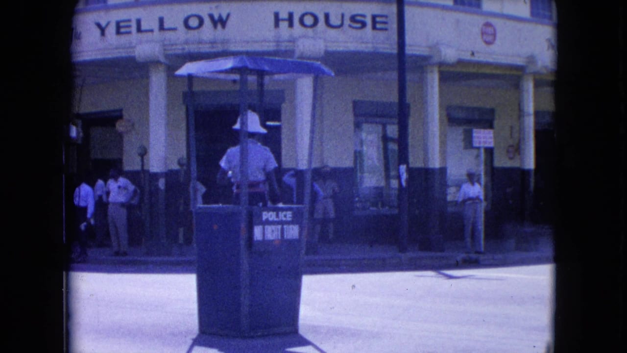 In Kingston, Jamaica, a police officer in white uniform stands in a blue booth marked for traffic control outside the Yellow House.