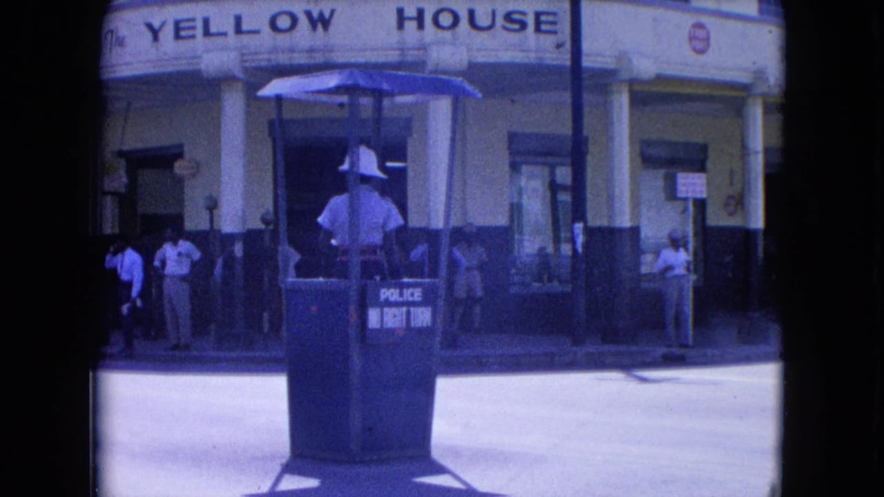 The officer stands facing the street from the blue booth while pedestrians gather near the Yellow House frontage in Kingston.