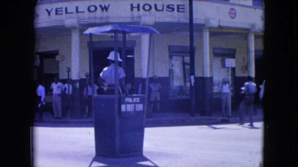 A Kingston street view shows the officer at the traffic booth, the Yellow House sign above, and several pedestrians along the sidewalk.