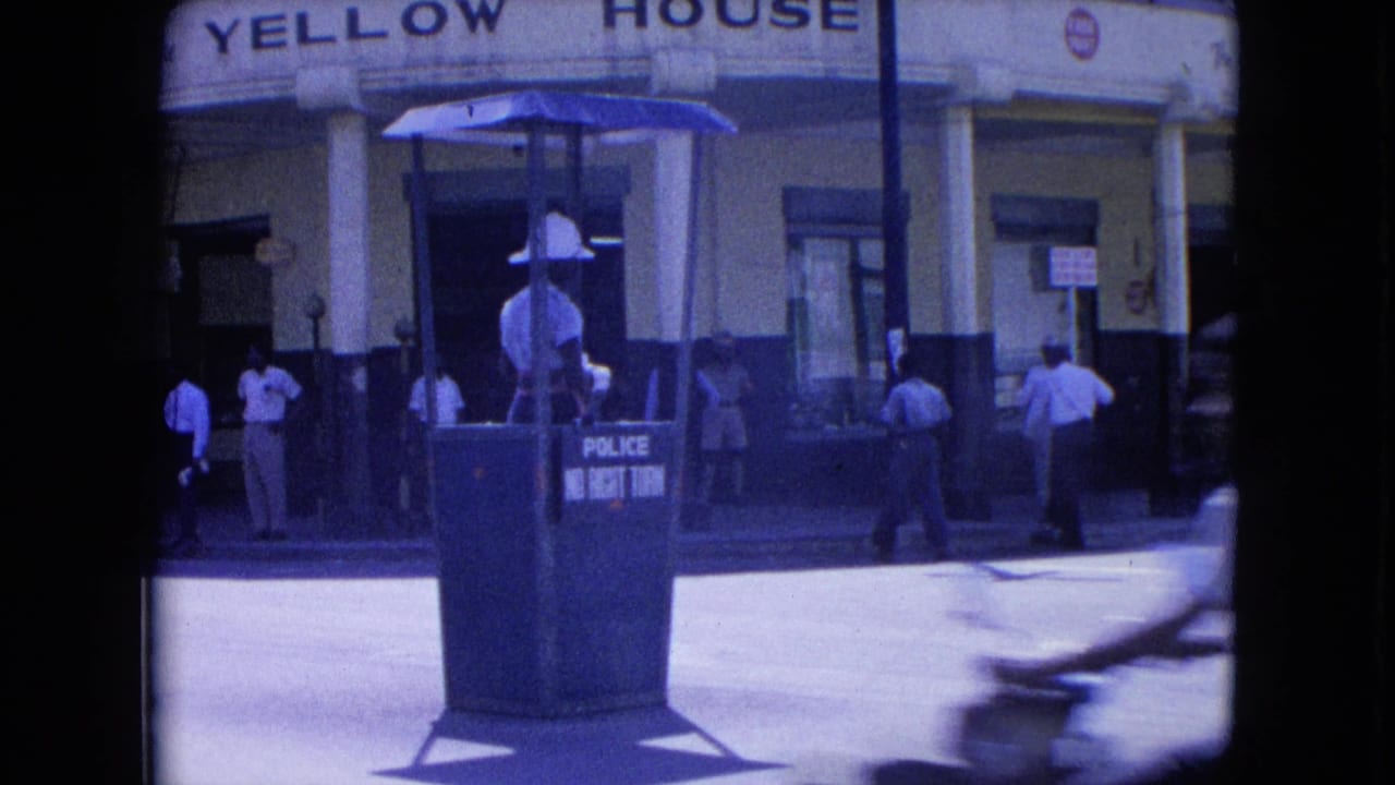 Police traffic guard stands in a booth outside Yellow House as pedestrians wait nearby.