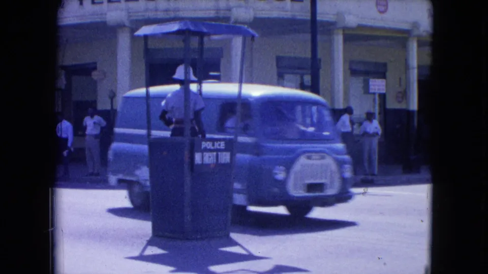 A blue van moves past the police traffic booth as pedestrians stand near the Yellow House building in Kingston.
