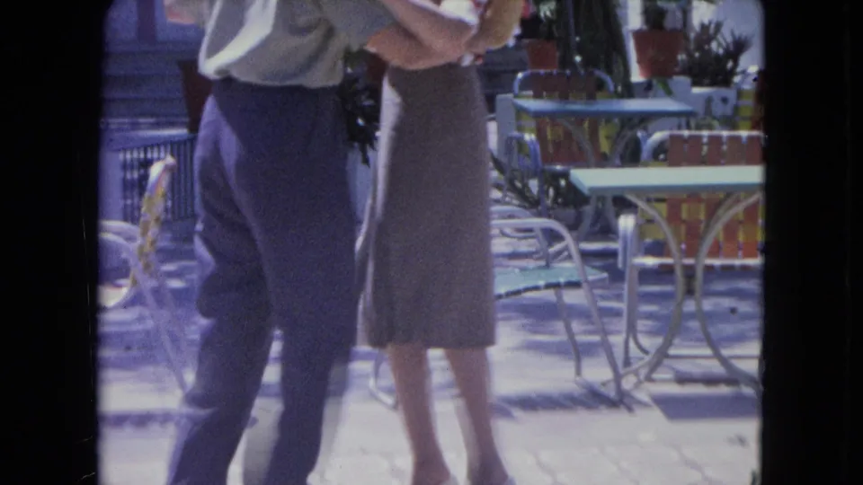 The home-movie frame captures the dancing pair on a Kingston patio, surrounded by painted metal chairs, tables, and plants.