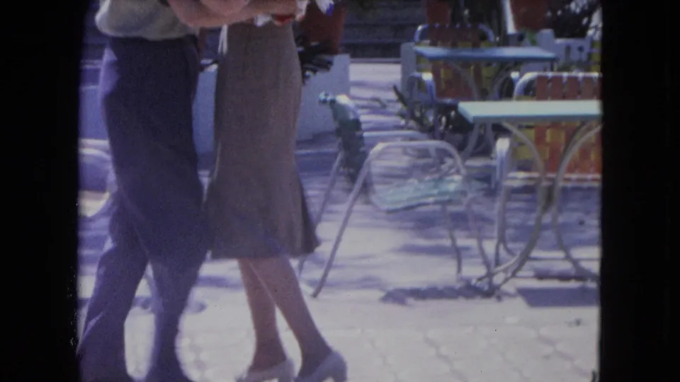 A 1964 Kingston home-movie frame shows the couple's lower bodies as they dance beside colorful outdoor furniture.