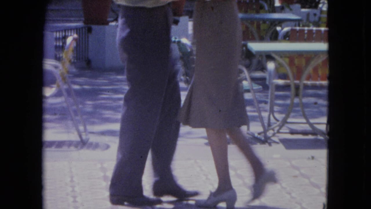In 1964 Kingston, Jamaica footage, a man and woman are framed from the waist down while dancing on a sunlit tiled patio.