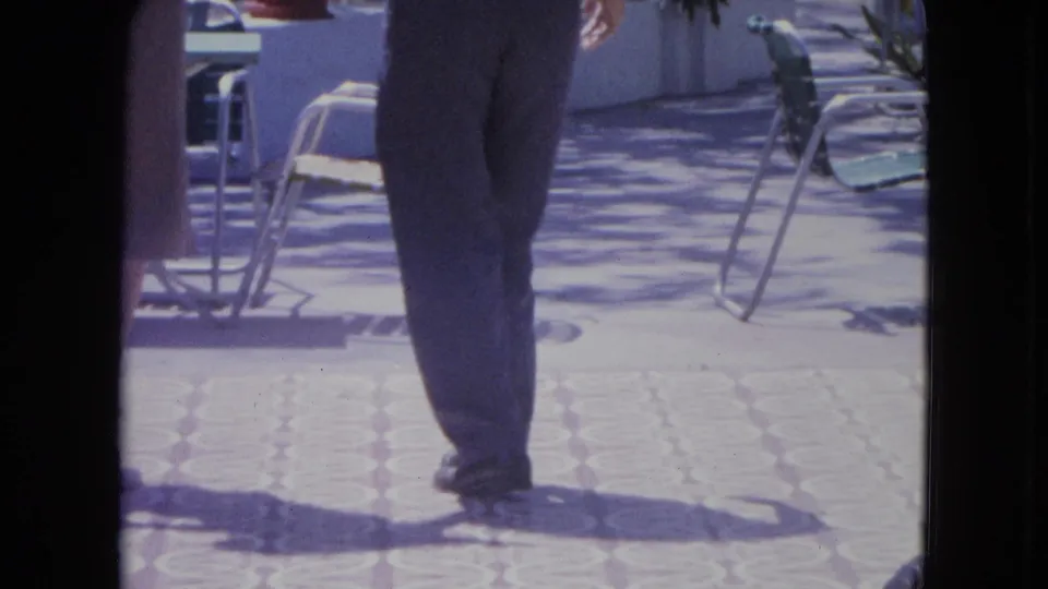 A waist-down frame centers on the man's trousered legs as the dance continues across a sunlit Kingston patio.
