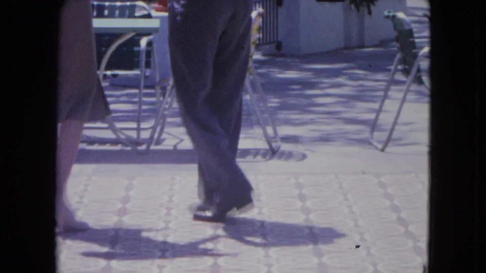 The dancers' legs overlap near the end of the clip, surrounded by metal patio furniture and strong afternoon-like shadows.