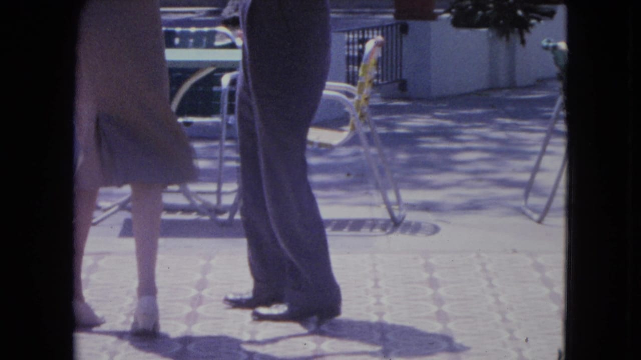 Lower bodies of a woman and man dancing on a sunlit tiled terrace near patio chairs.