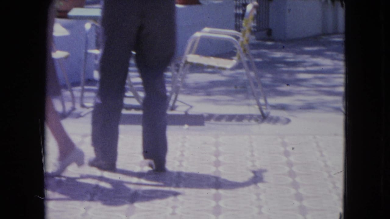 Dancers' legs and shadows move across patterned terrace tile beside folding chairs.