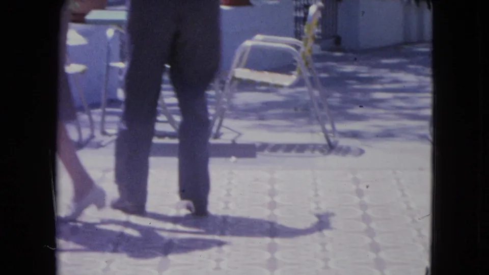 The couple continues dancing on a bright Kingston terrace, with the camera cropping them at the torso and emphasizing steps and shadows.