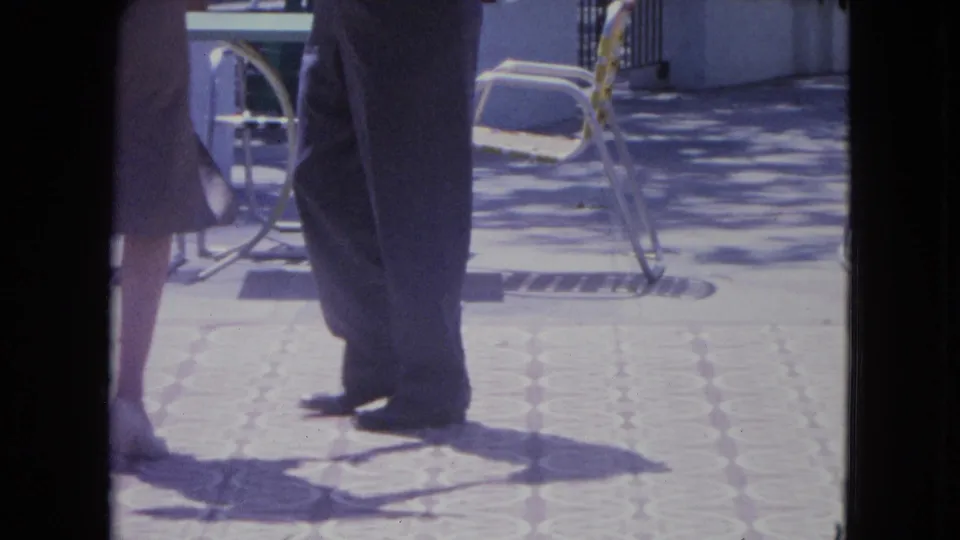 A cropped 8mm frame shows the woman and man stepping close together on the terrace, with patio chairs behind them.