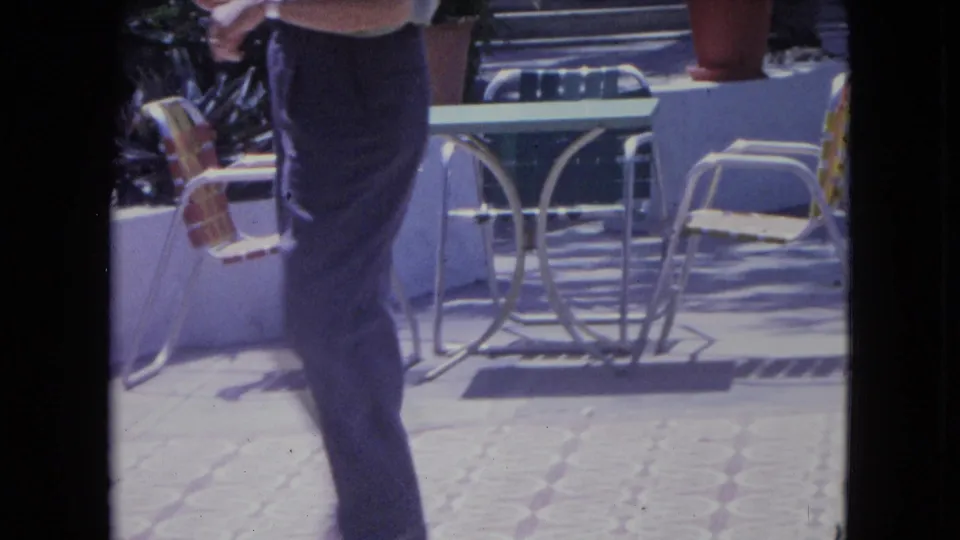 Near the end of the clip, the man moves across the Kingston terrace foreground with metal chairs, a table, and potted plants behind him.