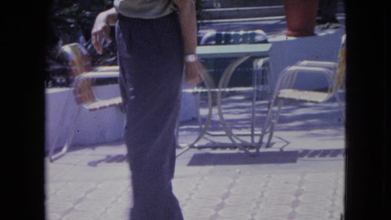 Two adults dancing on a sunlit patio beside metal tables and chairs.