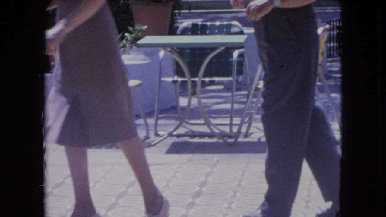 A woman in a knee-length dress dances near a man in trousers on a tiled patio.
