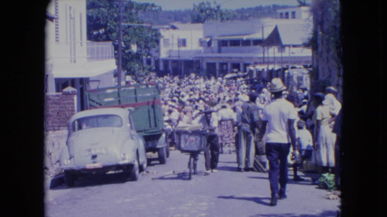 1964 Kingston, Jamaica street scene with a dense crowd, parked Beetle, green truck, and pedestrians moving through a market road.