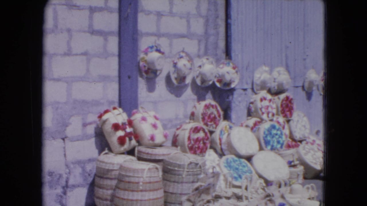Woven baskets and floral hats displayed on a sidewalk against a pale block wall.