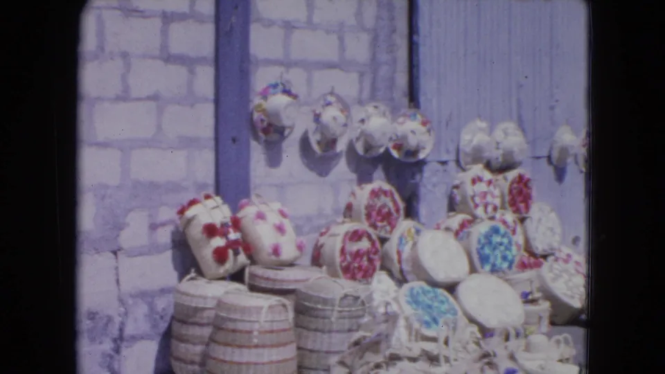 1964 Kingston, Jamaica market display with woven baskets, patterned hats, and craft goods arranged along a sidewalk.