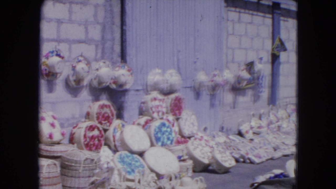 Street-market craft display with baskets, patterned hats, and pale wall behind.