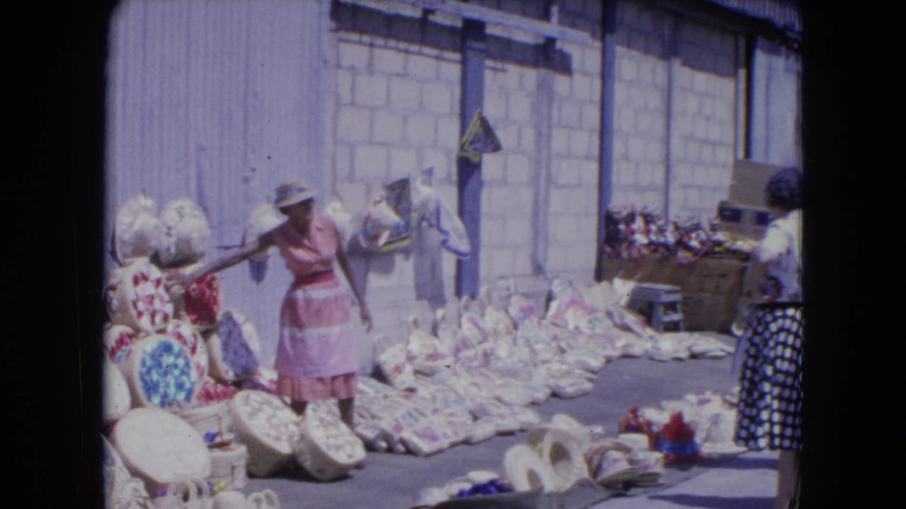 A Kingston street-market view shows a woman in pink gesturing near baskets as another shopper stands beside colorful goods.
