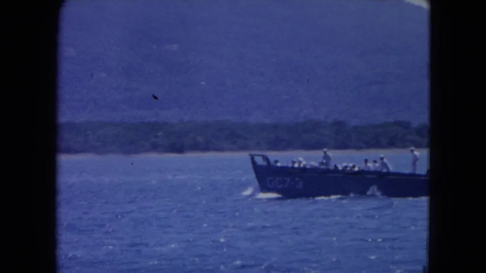 A boat with passengers travels across blue water near a distant shoreline, likely connected to the Kingston travel footage.