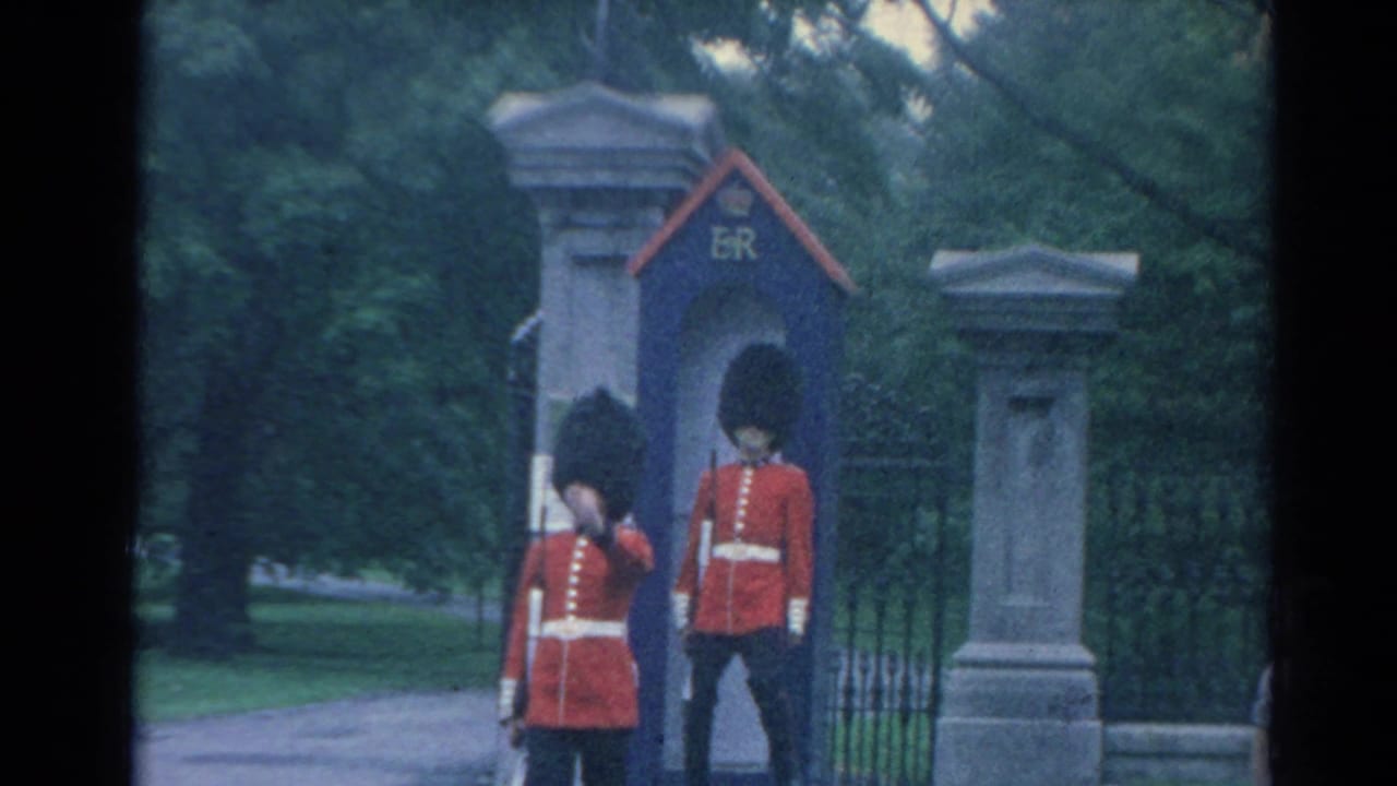 1964 London frame with two British ceremonial guards beside a blue sentry box marked ER at a gated entrance.