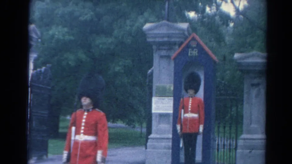 1964 London frame showing a red-coated guard walking past a blue ER sentry box where another guard stands at attention.