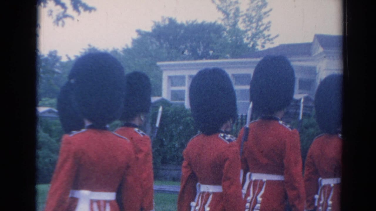 Rear view of guards in red tunics walking in formation near a building.