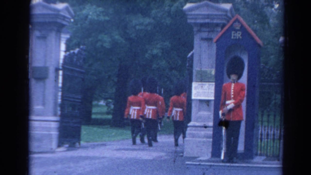 1964 London footage showing guards in red tunics marching away as a sentry stands beside a blue ER-marked box at a stone gate.