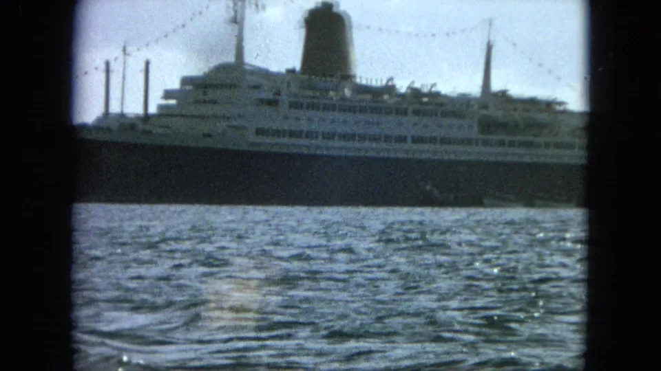 The ship fills more of the frame in a broadside view, showing stacked decks, a dark hull, funnel, masts, and water in the foreground.