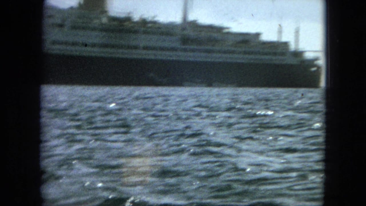 A large passenger ship appears on sunlit water in soft, grainy 8mm footage from a tourist vantage point.