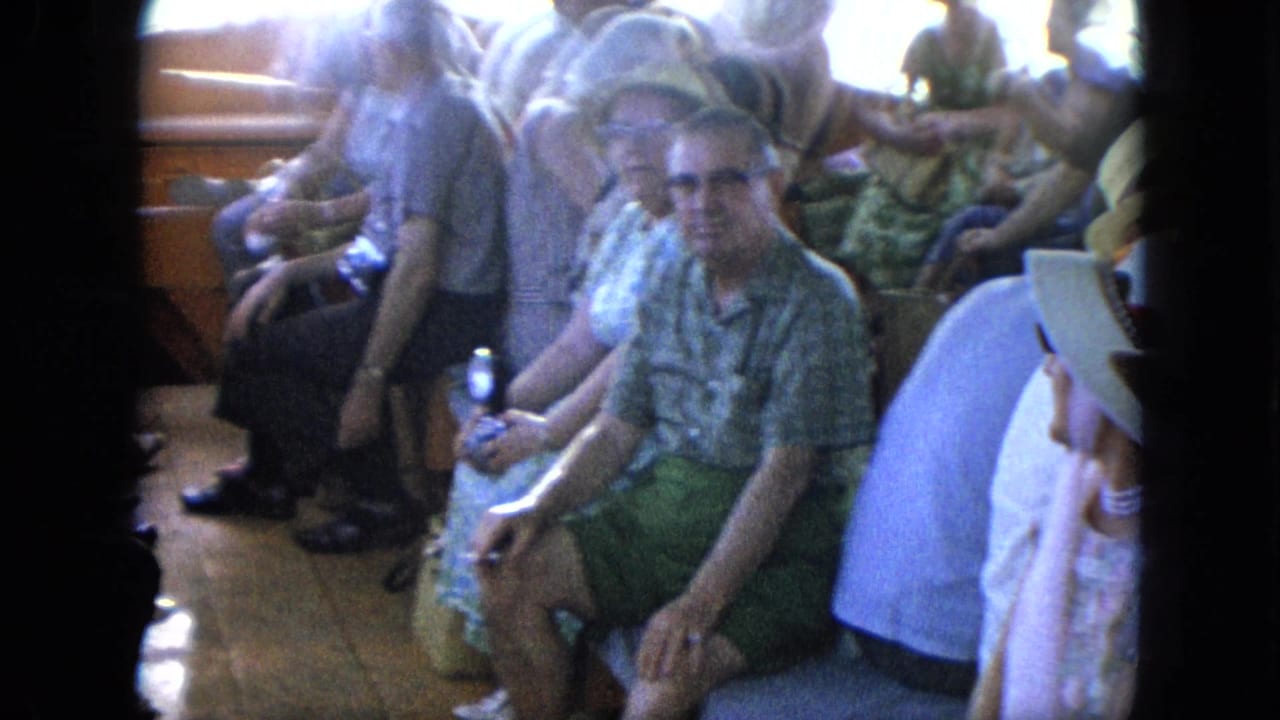 Passengers seated closely on a boat, with a man in sunglasses looking toward the camera.