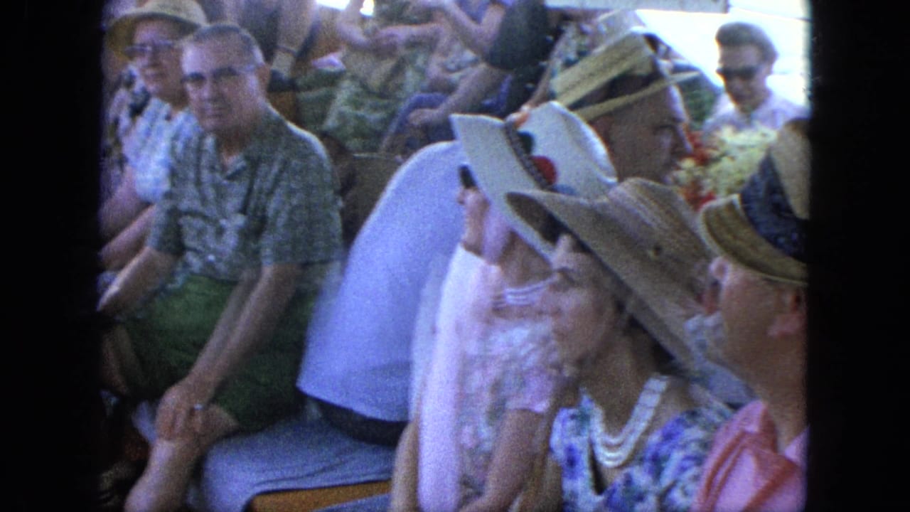 Boat passengers in hats and summer clothing sit near the water-facing side of the vessel.
